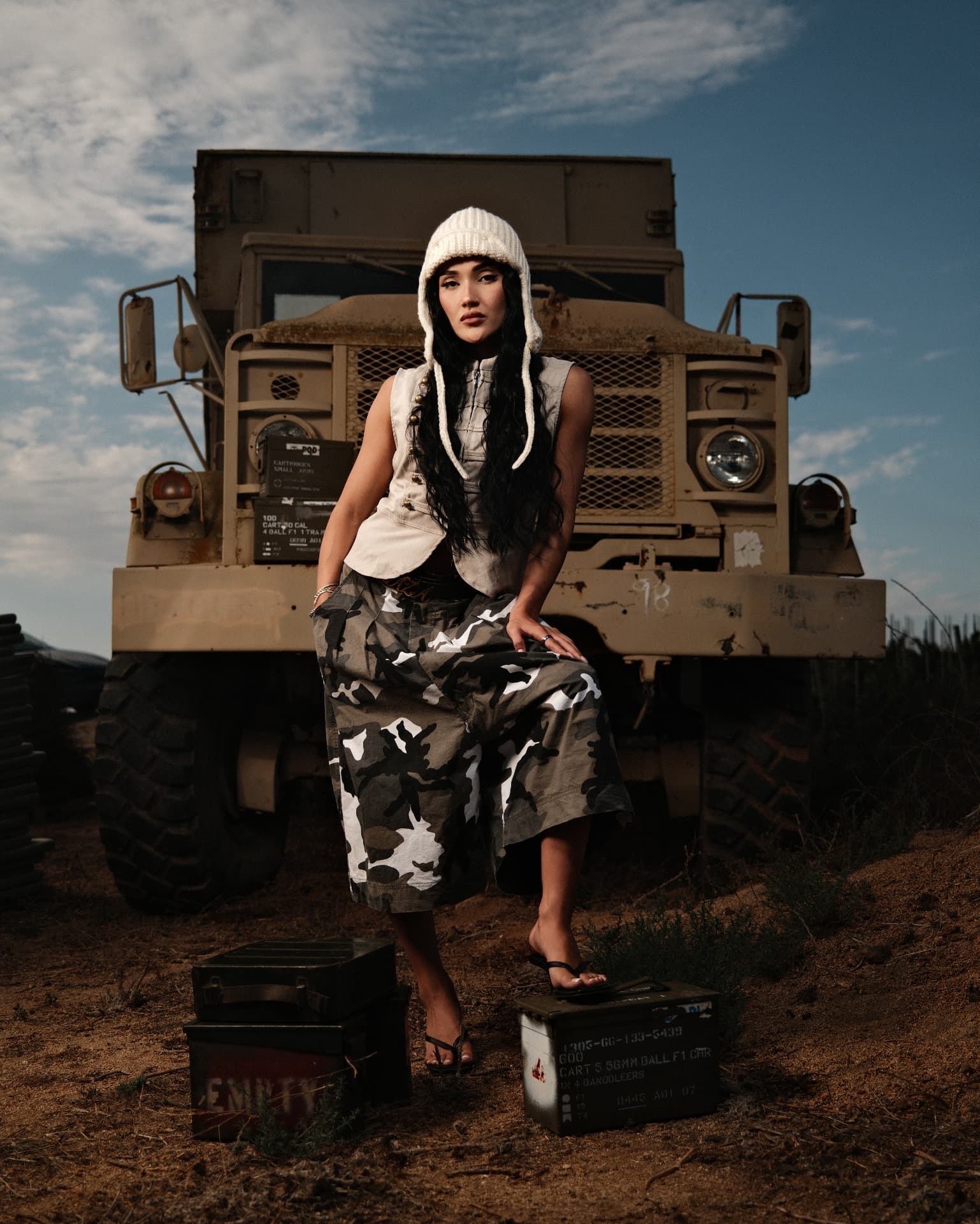 Portrait in a white knit hood and camo trousers beside a military transport truck
