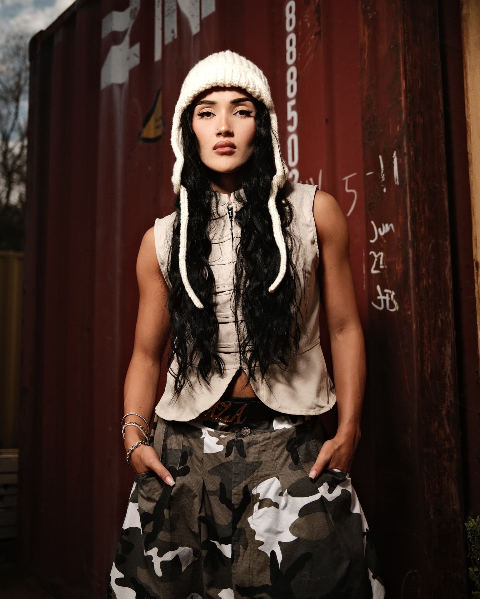 Portrait in a knit hood and vest against a red shipping container